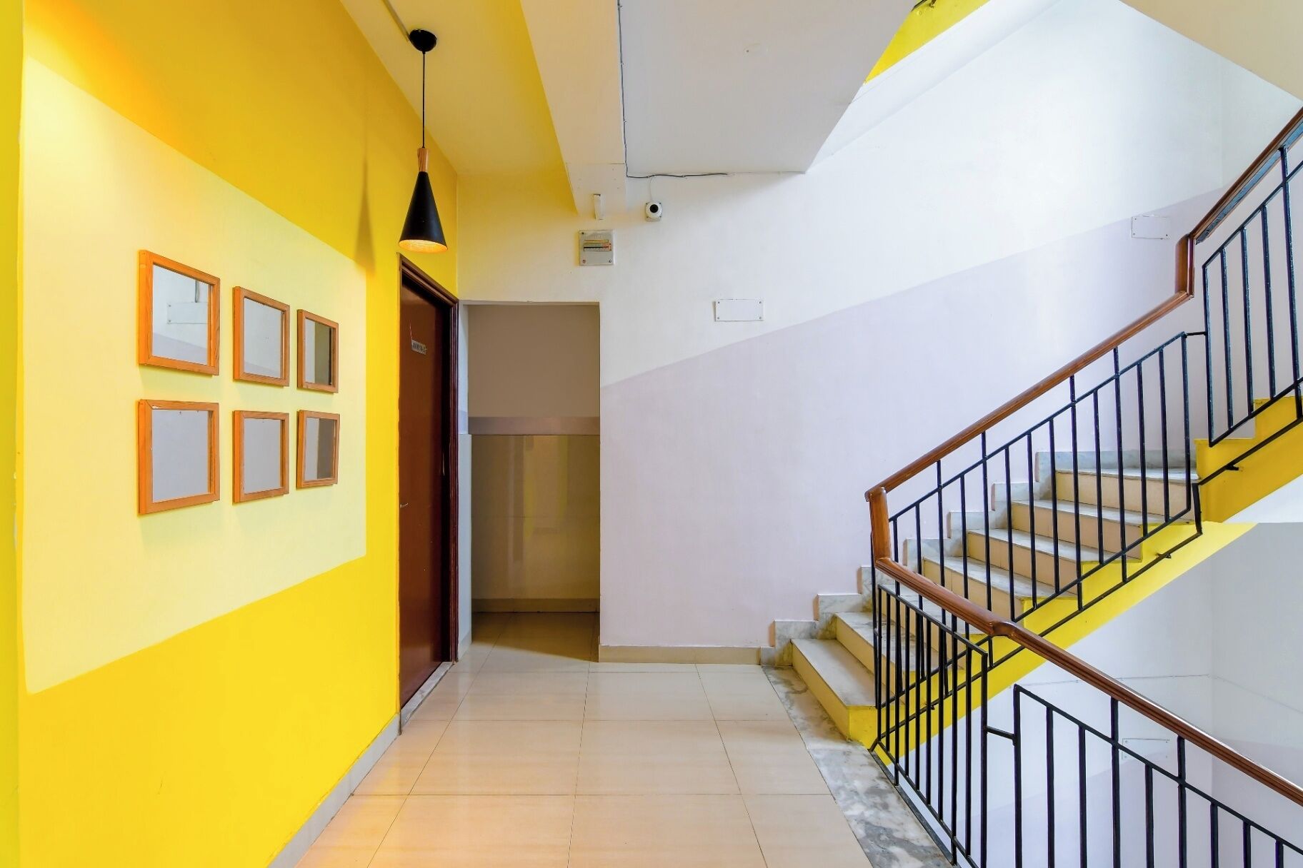 A hallway with a yellow wall, a staircase with a black railing, and a door leading to another room.