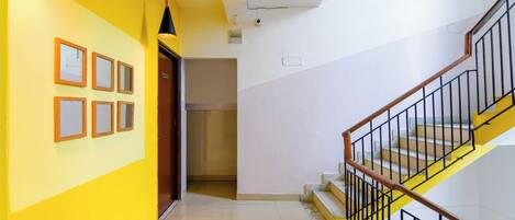 A hallway with a yellow wall, a staircase with a black railing, and a door leading to another room.