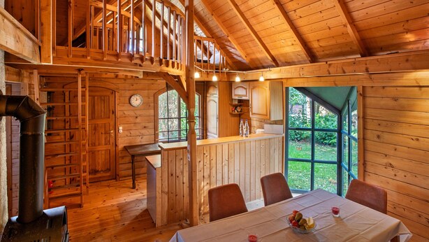 Interior de una cabaña de madera con comedor, cocina y habitación en altillo.
