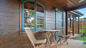 Fachada de madera con un porche cubierto, dos sillas de madera y una mesa.