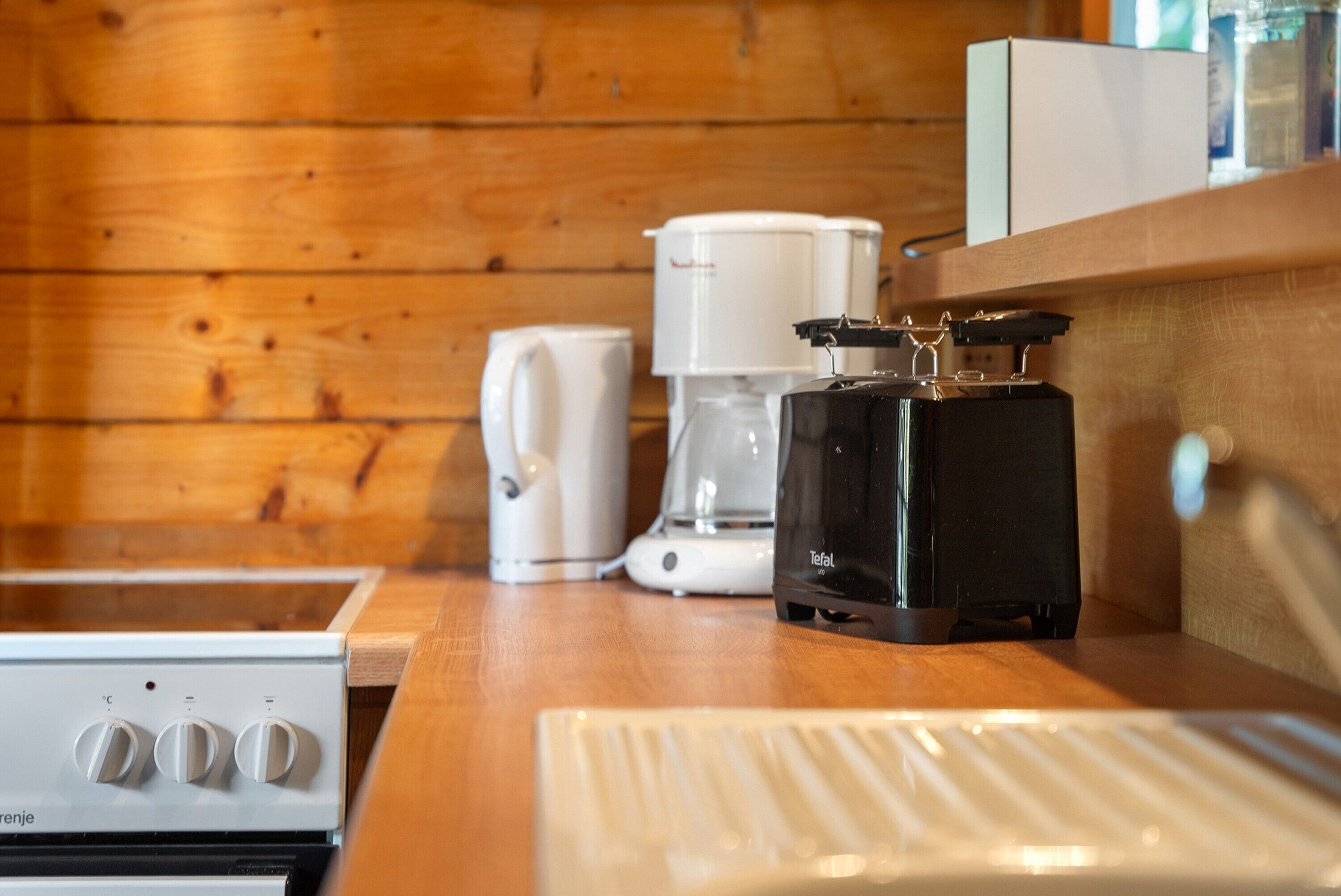 Une petite cuisine équipée d’une machine à café, d’une bouilloire et d’un grille-pain, le tout posé sur un plan de travail en bois.
