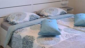 Un dormitorio con cama, almohadas, una mesita de noche, una lámpara de pared y una obra de arte floral.