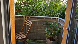 Une chaise en bois appuyée contre une clôture, une plante en pot et une vue sur la verdure et les bâtiments.