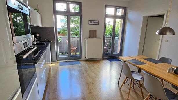 Une cuisine moderne dotée d’un four encastré et d’un coin repas avec une table et des chaises en bois.