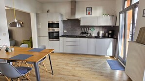 Une cuisine moderne avec des meubles blancs, une table à manger en bois et une grande fenêtre.