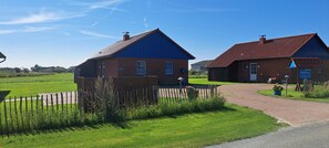 A rural setting with two brick buildings, a wooden fence, and a paved path. - Holiday Home 'Springflut' with Shared Garden and Wi-Fi (Pellworm)