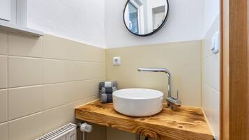 A bathroom with a round white sink, a wooden countertop, a mirror, and a towel.