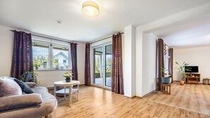 Ein Wohnzimmer mit einer Couch, einem kleinen runden Tisch, einer TV-Konsole mit Fernseher und Holzboden.