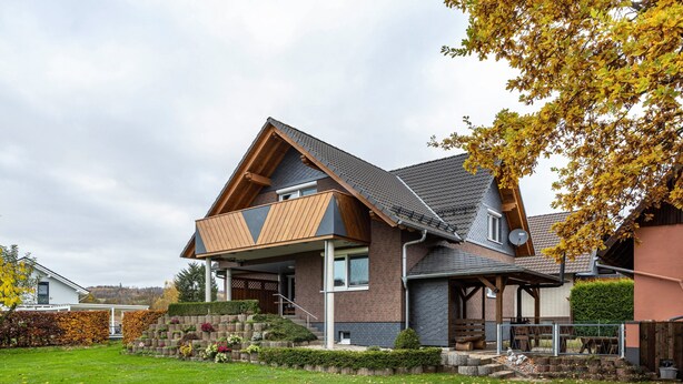 Ein modernes Haus mit Satteldach, einer überdachten Veranda und einem gepflegten Garten.