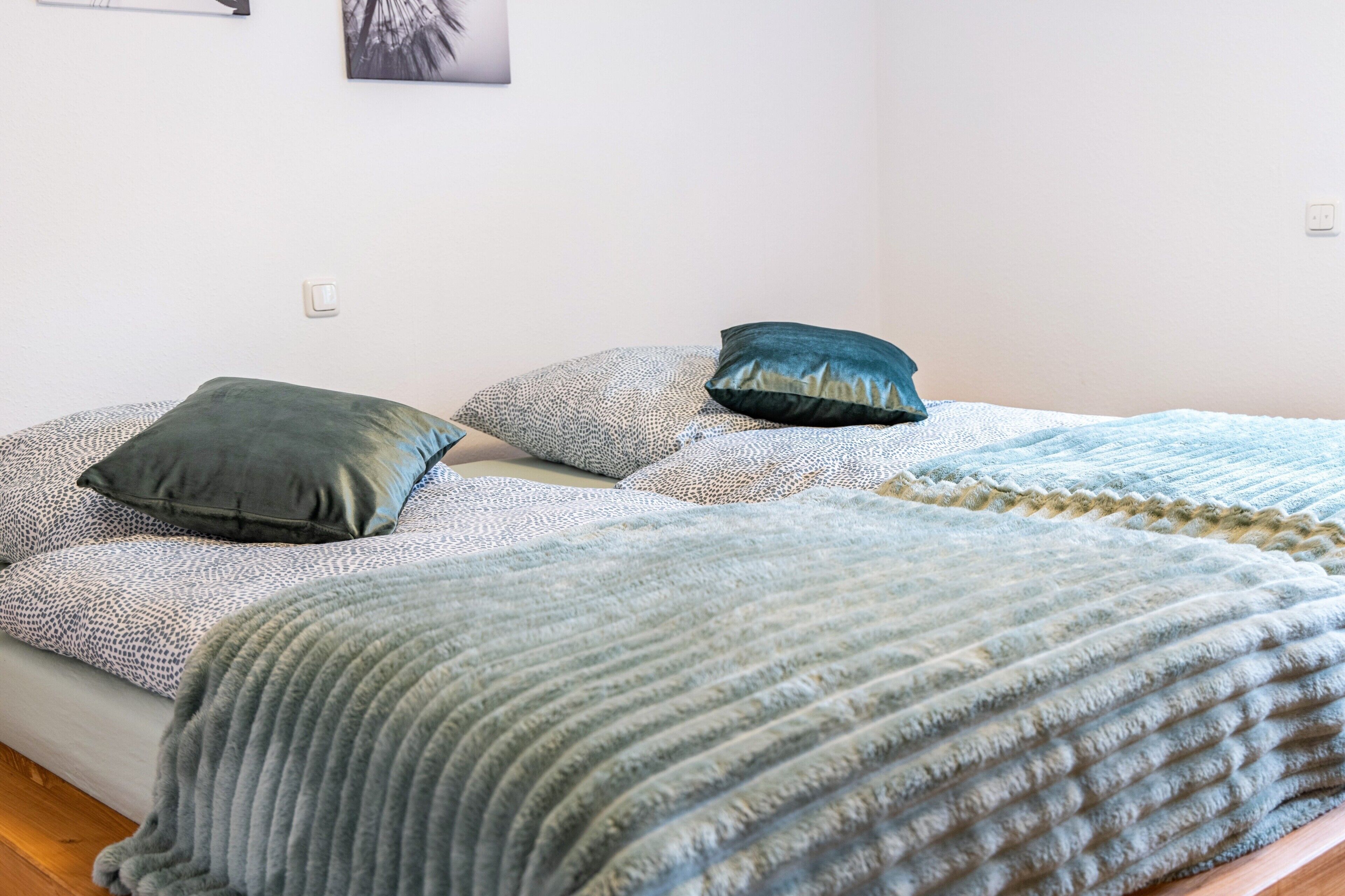 Een bed met beddengoed en kussens met een patroon, een muur met lichtschakelaar, en een ingelijst foto.