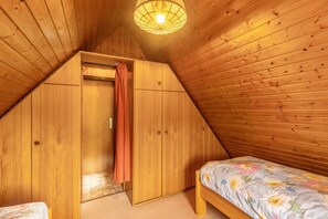 Une chambre avec un plafond en pente, des murs en bois, un lit avec une literie à motifs floraux et un luminaire suspendu.