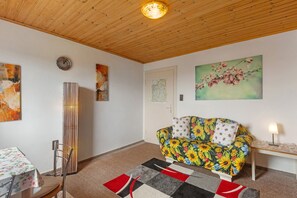 Une pièce avec un plafond en bois, un canapé recouvert d’un tissu à motifs floraux, une table à manger avec une nappe à motifs floraux et un tapis à motifs.