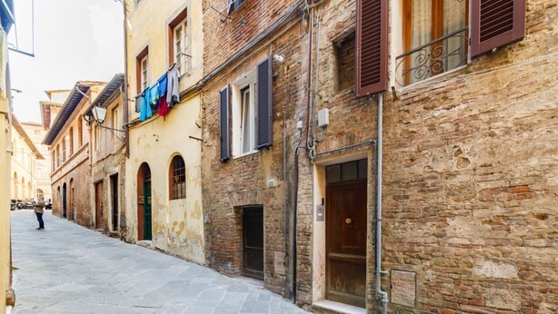 A narrow street with historic buildings, stone pavement, and a person walking.
