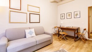 A living room with a sofa, a dining table with chairs, and framed pictures on the wall.