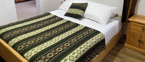 Ein Einzelbett mit einem gemusterten Bettbezug, ein Nachttisch aus Holz und ein Fenster mit Vorhängen.