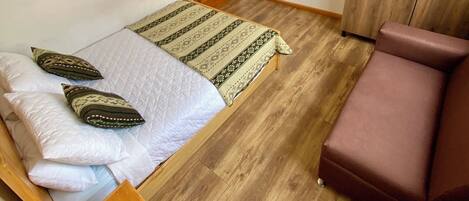 A small, clean room with a bed, a wooden cabinet, a television, and a small table.