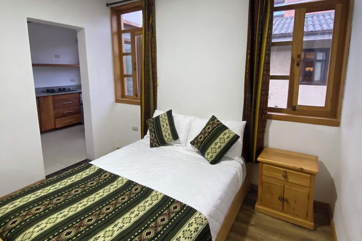 A bedroom with a bed, a wooden nightstand, a wardrobe, and a window with curtains.