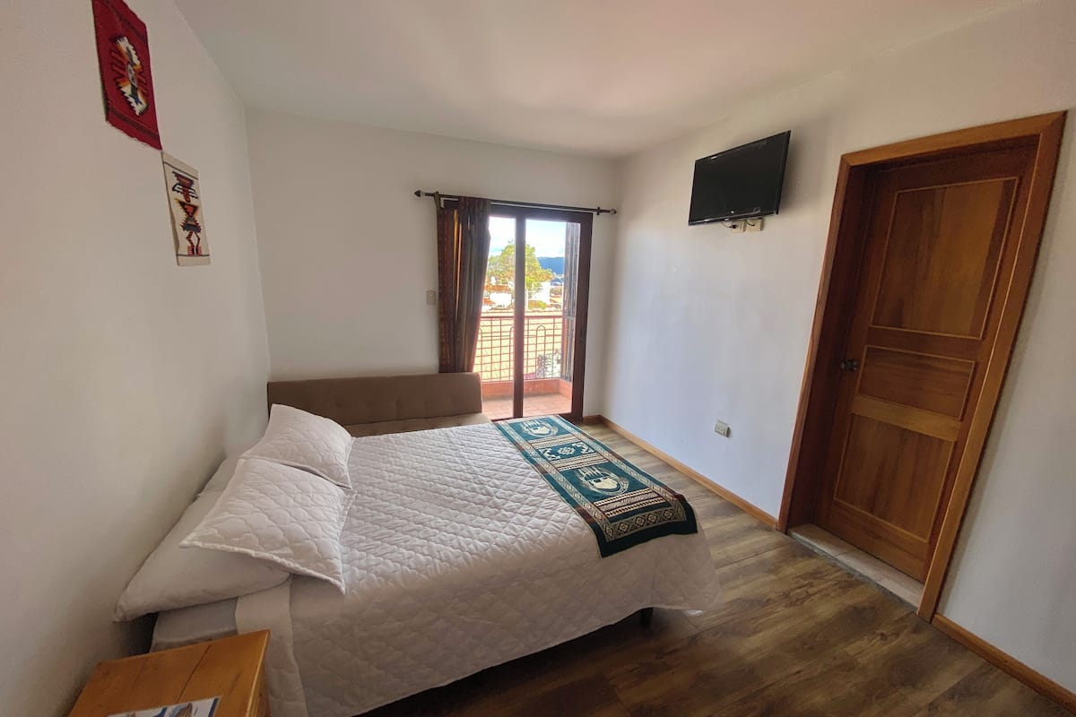 A bedroom with a bed, a wooden floor, a TV mounted on the wall, and a sliding door.