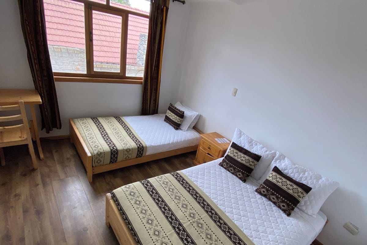 A bedroom with two single beds, a wooden desk, and a window with curtains.