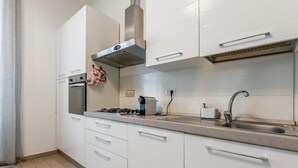Ett modernt kök med vita skåp, en spishäll i rostfritt stål, en inbyggd ugn, en gasspis, en diskho och en köksfläkt.