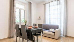 En matplats med ett bord dukat för fyra personer, en soffa och ett fönster med gardiner.