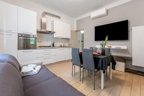 Une cuisine moderne avec des meubles blancs, un four encastré et un coin repas comprenant une table et des chaises.