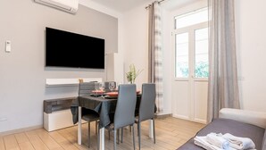 Ett modernt vardagsrum med en platt-TV, matbord, stolar och en soffa.