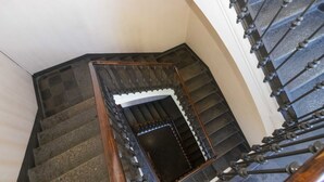 A staircase with a wooden handrail and metal balusters, leading to a landing with a dark-colored door. - GuestHost - San Donato & Piazza Statuto Appt x3 with Balcony (Torino)