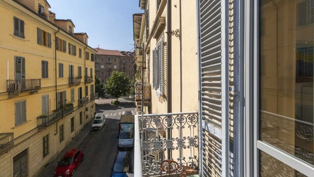 A narrow street with buildings on either side, a red car parked on the left, and a blue car on the right. - GuestHost - San Donato & Piazza Statuto Appt x3 with Balcony (Torino)