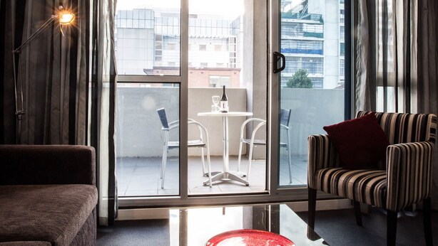 Een moderne woonkamer met een bank, een gestreept fauteuil en een glazen deur die leidt naar een buitenbalkon met een tafel en stoelen.