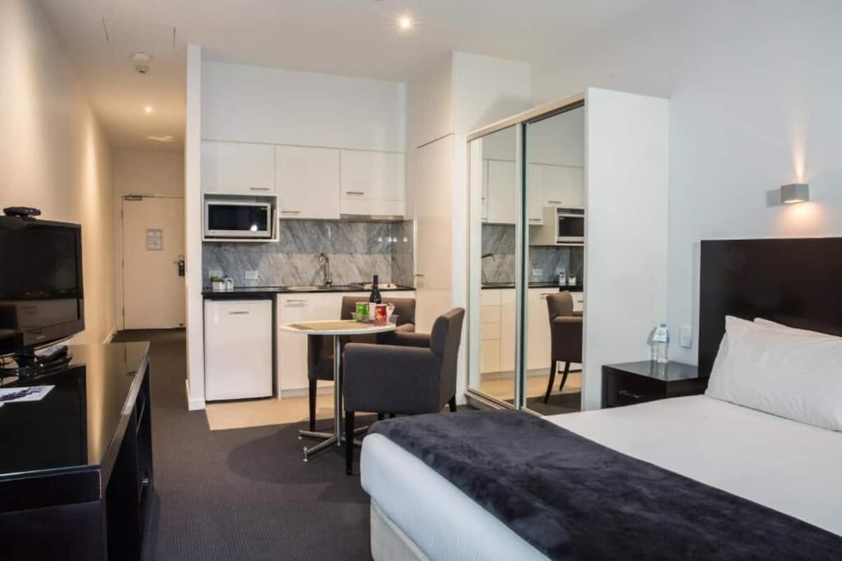 Habitación de hotel con cama, escritorio con silla, televisor, microondas y pequeña cocina.
