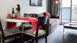 Een moderne woonkamer met een ronde eettafel, gestreepte stoelen, een grijze bank met rode kussens en een groot raam met gordijnen.