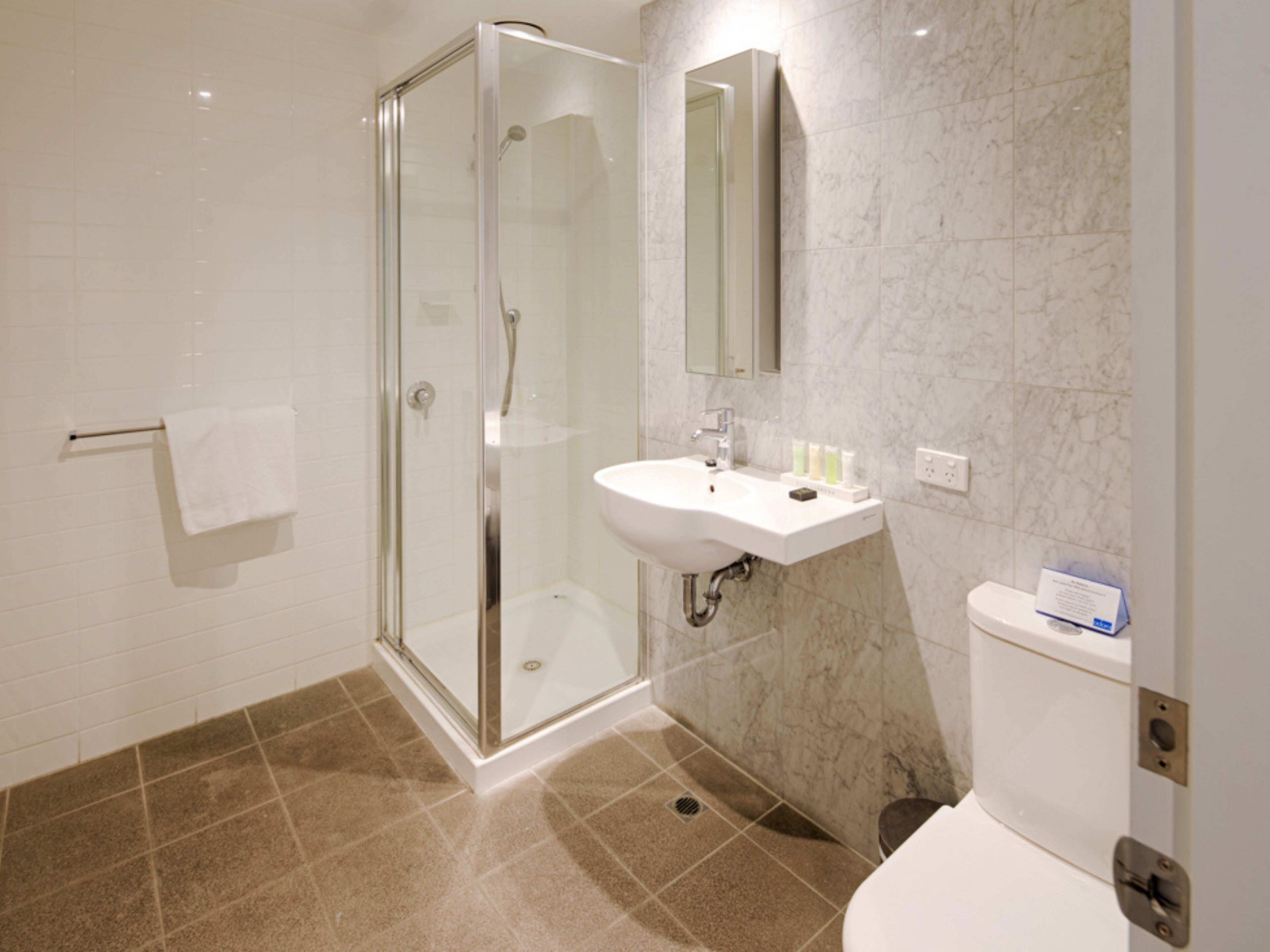 Un baño moderno con cabina de ducha de vidrio, un lavamanos blanco y suelo de baldosas de mármol.