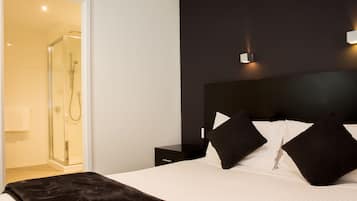 A modern hotel room with a large bed, a dark headboard, and a glass shower enclosure.
