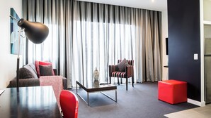 Een moderne woonkamer met een bank, fauteuil, salontafel en een rode poef.