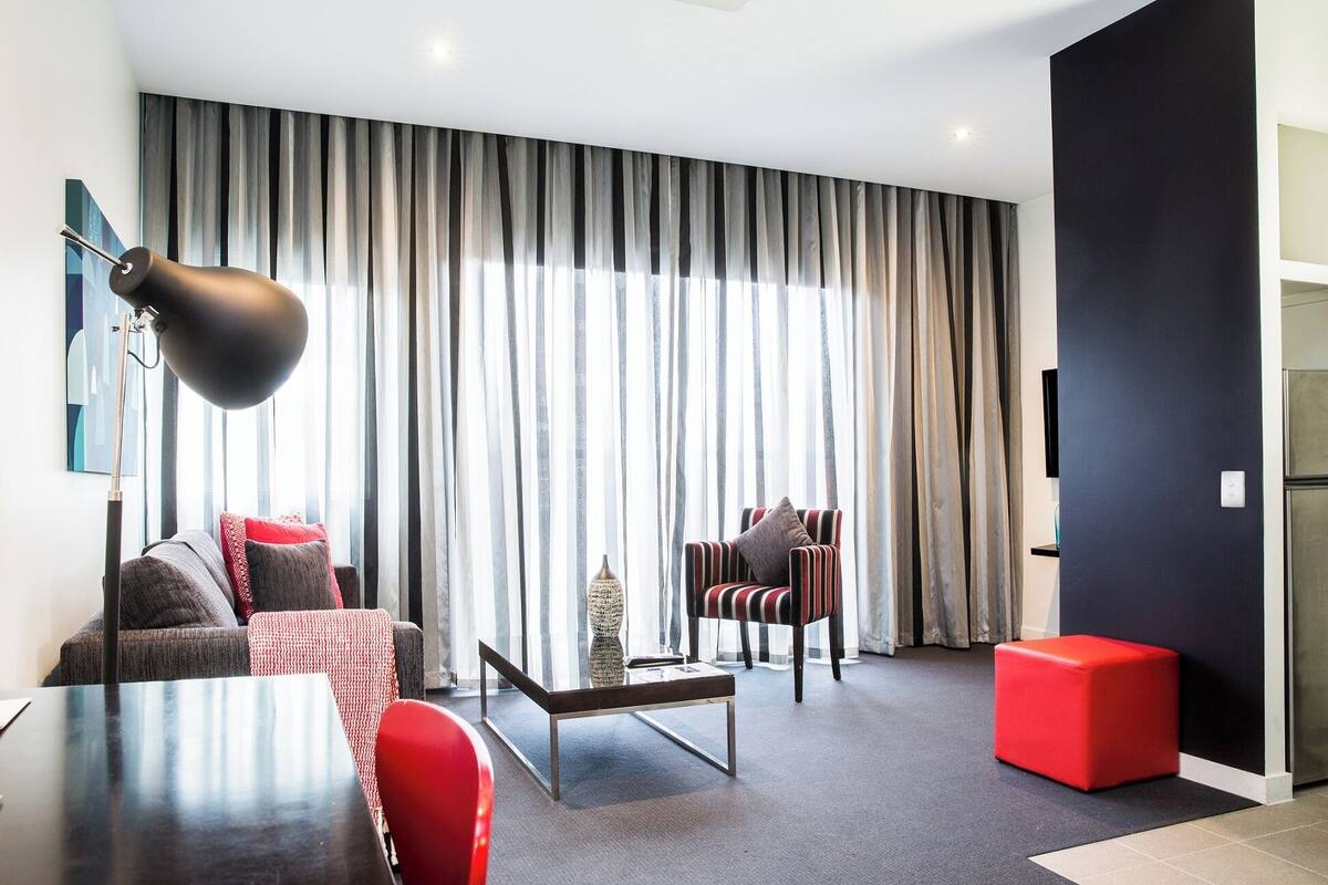 Una sala moderna con un sofá, un sillón, una mesa de centro y un otoman rojo.