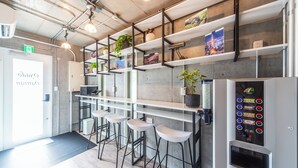 Un espace bar moderne avec des tabourets blancs, des étagères ornées de plantes et de livres, et un distributeur de boissons.