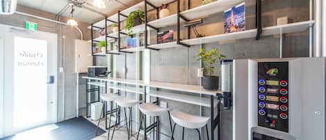 Eine moderne Bar mit weißen Hocker, Pflanzen und Büchern auf Regalen und einem Getränkespender.