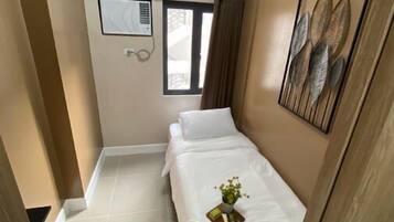 A small, well-lit bedroom with a bed, a window, and a wall-mounted air conditioning unit.