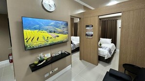 Een hotelkamer met een flatscreen televisie, een klok, een bord met voorzieningen en een bed.