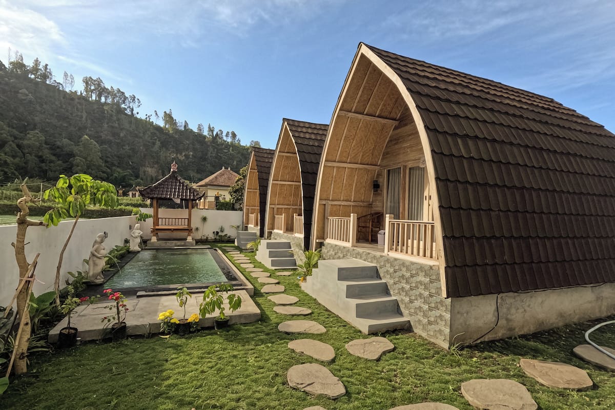 A modern building with a curved roof, a swimming pool, and a stone pathway leading to the entrance.
