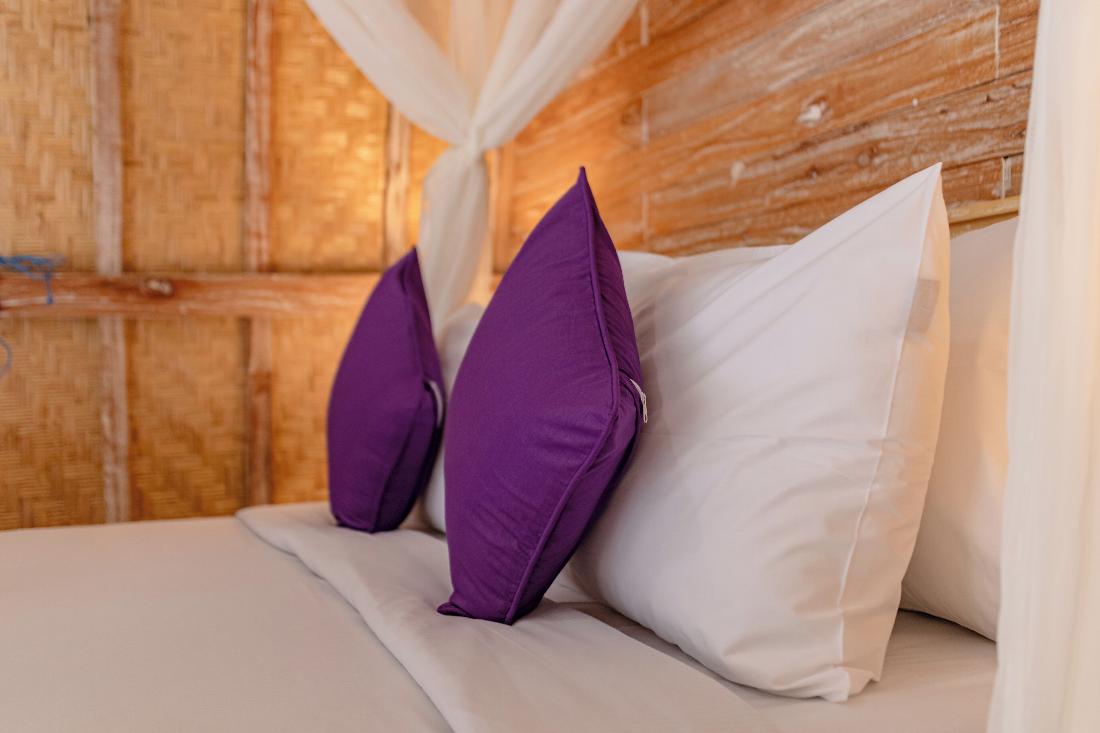 Una cama con almohadas blancas y moradas, un cabecero de madera y un dosel blanco.