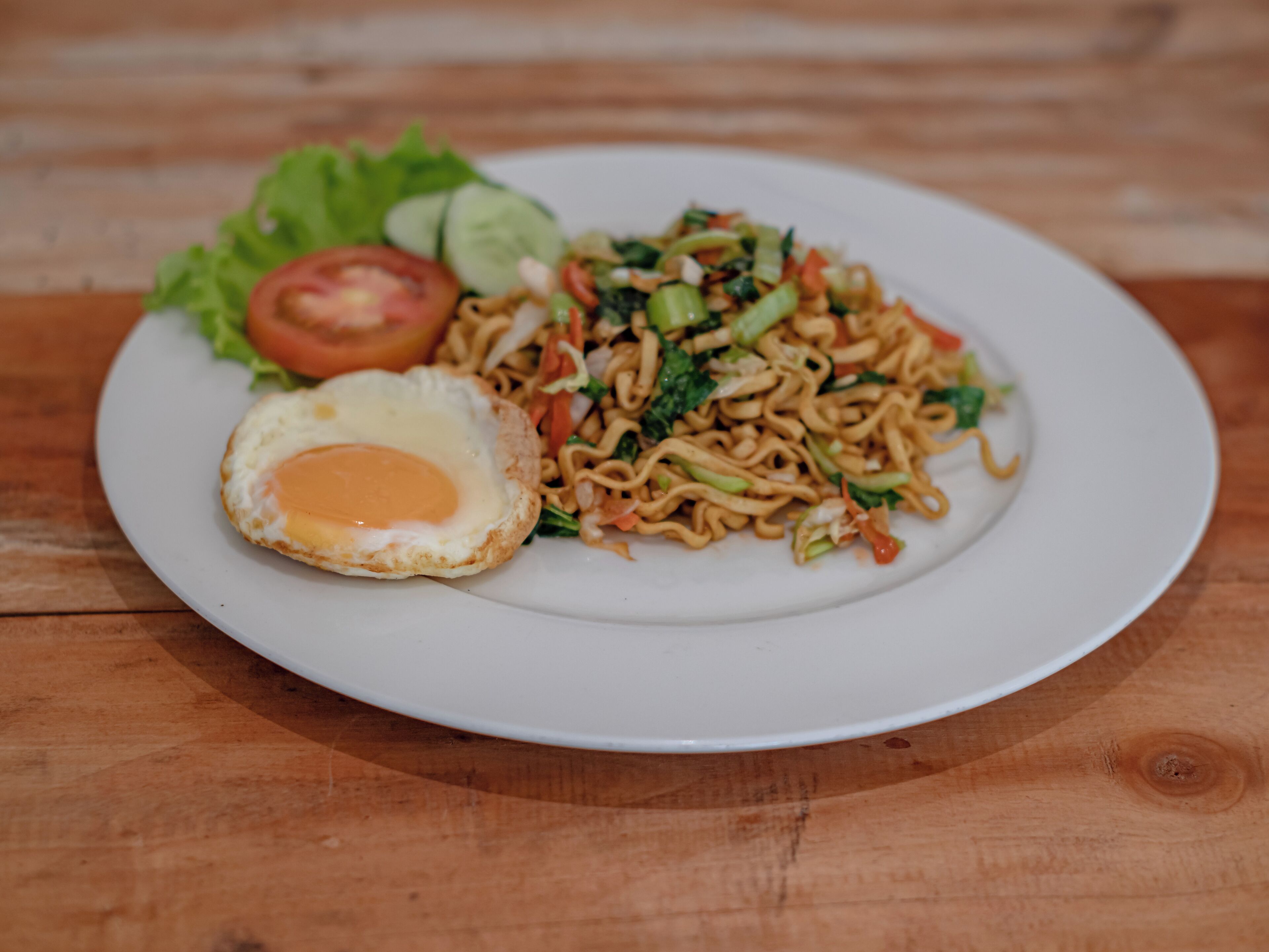 A plate of noodles with vegetables and a fried egg on a white plate.