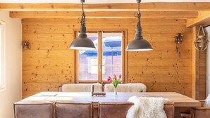 A wooden-paneled room with a dining table, chairs, and two hanging lamps.