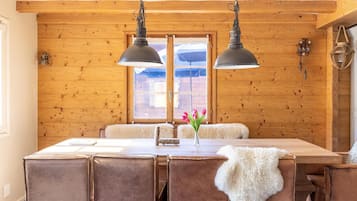 Een kamer met houten lambrisering, een eettafel, stoelen en twee hanglampen.