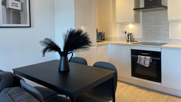 A modern kitchen with a dining area, featuring a black vase with black feathers, a coffee machine, and a built-in oven. - 2 Bed with Wi‑Fi, Near Central Birmingham (Birmingham)