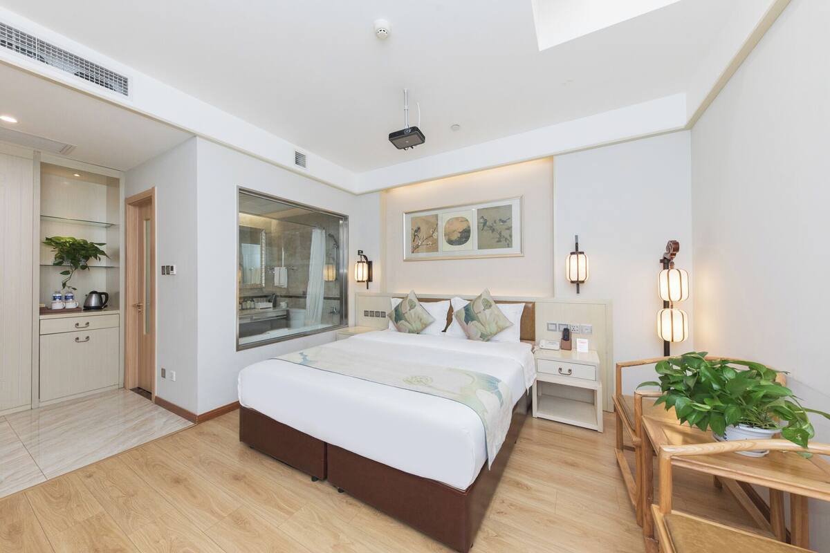 A modern bedroom with a large bed, bedside tables, a desk, and a view of the bathroom.