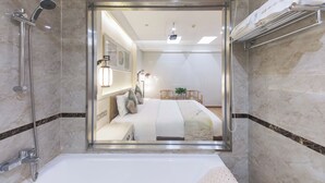 A modern bathroom with a glass-enclosed shower, a bathtub, and a bed visible through the glass. - Yitingzhenshe Hotel Beijing Tiananmen (Beijing)