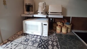 A compact kitchen with a microwave, coffee maker, and blender on a shelf.