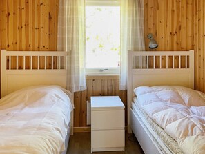 A room with two beds, a small white nightstand, and a window with curtains.